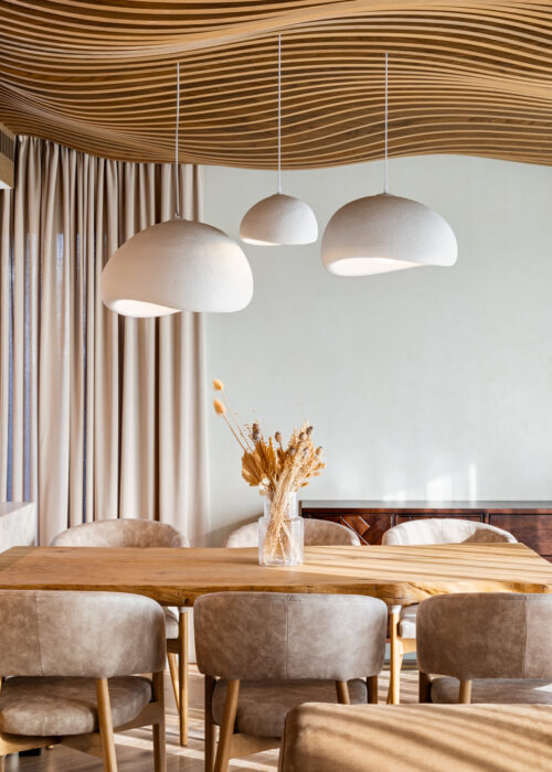 Dining area under the Airwood wave ceiling, three white boucle pendant lamps over a live-edge wood table