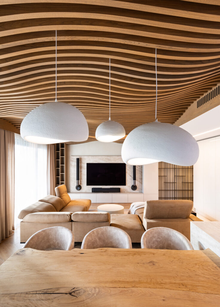 Living room seen from the dining table, the wave-form wooden ceiling and white pendant lamps overhead