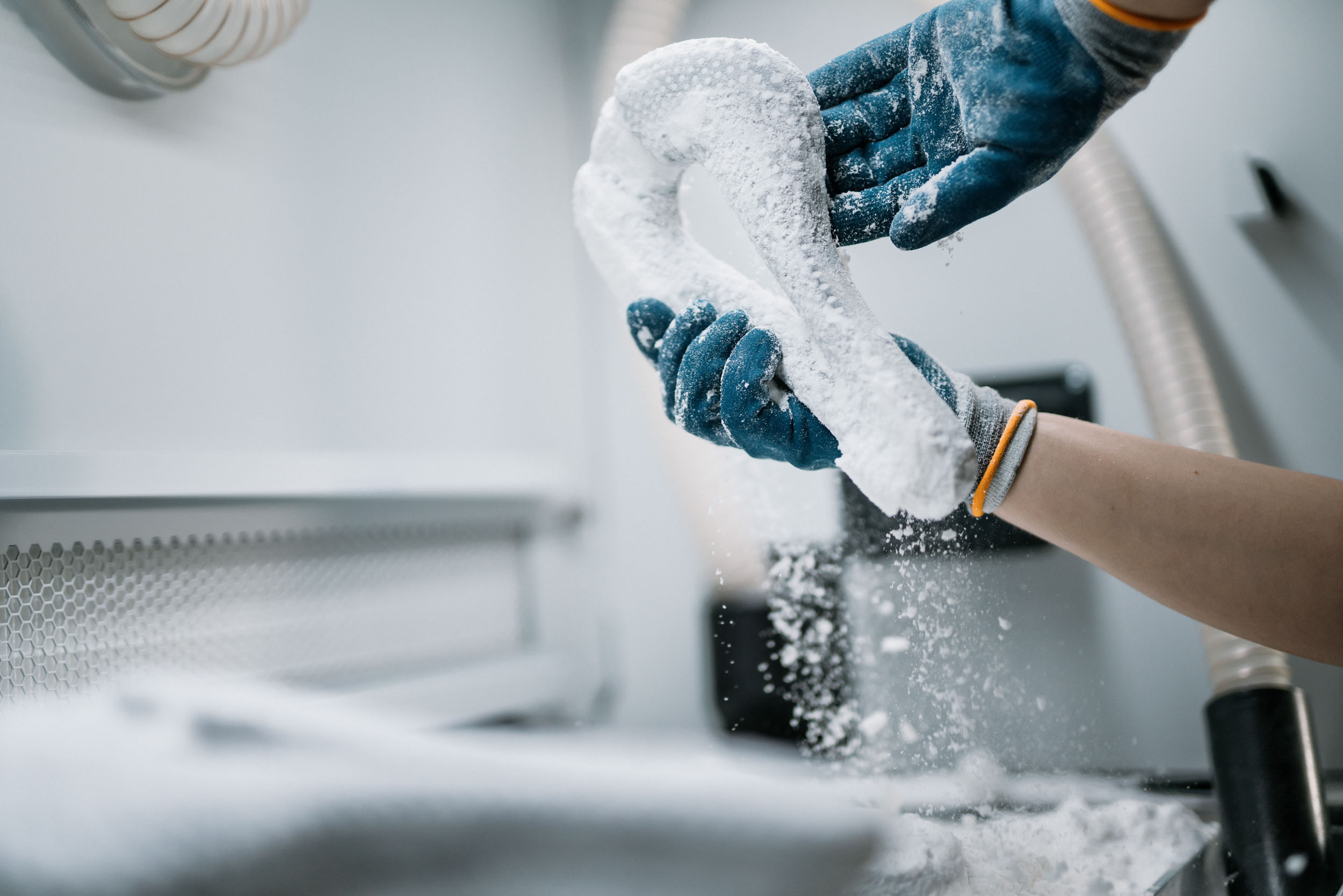 Raw white nylon Joyseat print being cleaned of powder by gloved hands at the post-processing station