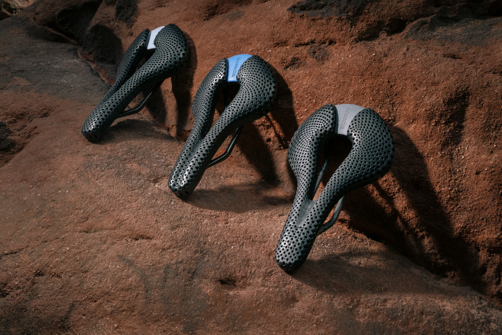 Three black 3D-printed Posedla Joyseat cycling saddles standing on red sandstone rock