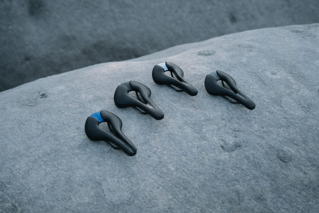 Five black 3D-printed Posedla Joyseat saddles arranged on a smooth grey boulder